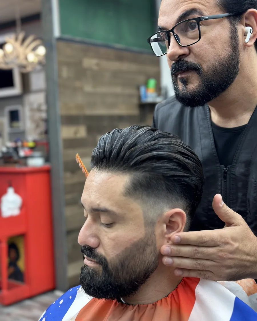 A barber shaping a client's beard by hand