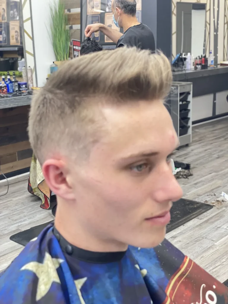 Blond man with a quiff and a skin fade, seated in the barber chair