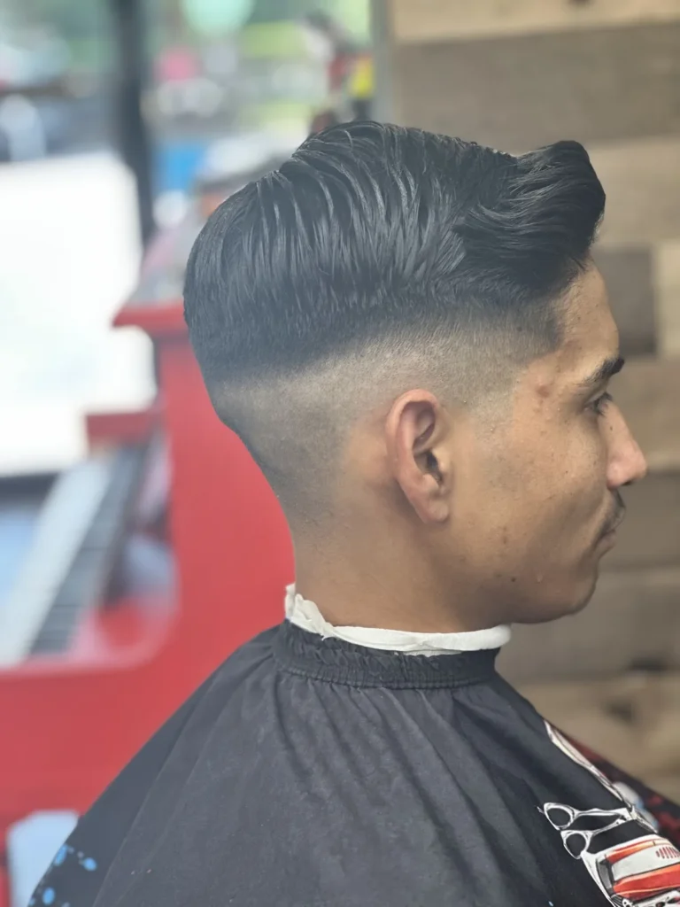 Man with a brushed-back top and a mid fade, the shop’s red piano behind him