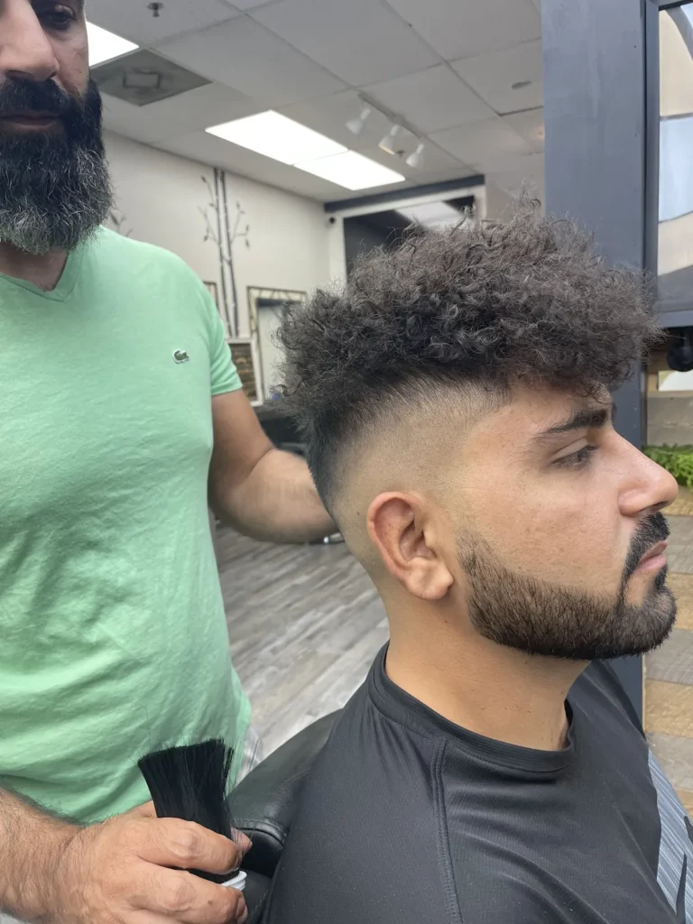 Man with curly hair, a burst fade and a trimmed beard, brushed off after the cut