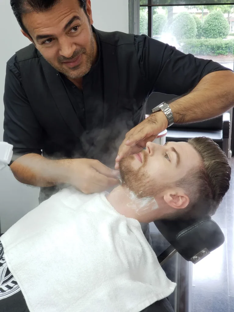 Barber laying a steaming hot towel over a reclined customer’s face